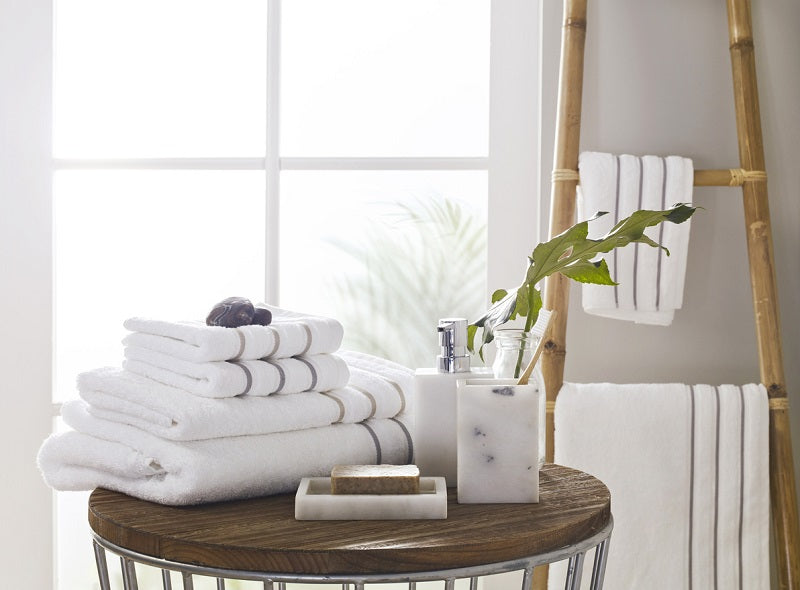Stacked white bath towels on a small table beside a towel ladder