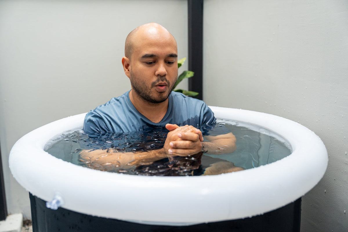 Man seated in an indoor cold plunge tub, hands clasped, breathing slowly