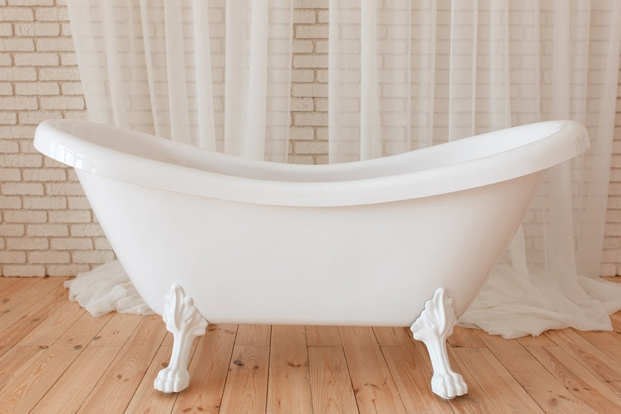 White acrylic clawfoot tub on a wood floor in front of sheer curtains