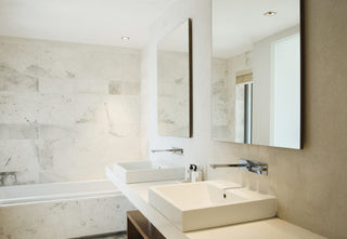 Two square basins on a floating counter in a pale limestone bathroom