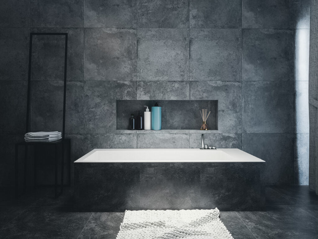 White tub set into a dark concrete tiled surround below a long recessed niche