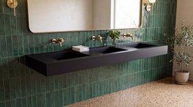 90" ADA Triple Ramp Sink, Wall Mounted in matte black with brass faucets in a green-tiled hotel bathroom, open space underneath