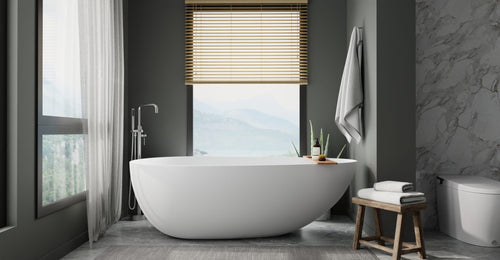 Badeloft BW-01-XXL freestanding bathtub in matte white by a tall window with a mountain view, a wood stool and dark walls