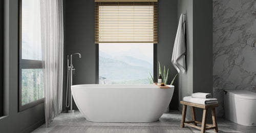 Badeloft BW-02-L freestanding bathtub in matte white by a tall window with a mountain view, a wood stool and dark walls